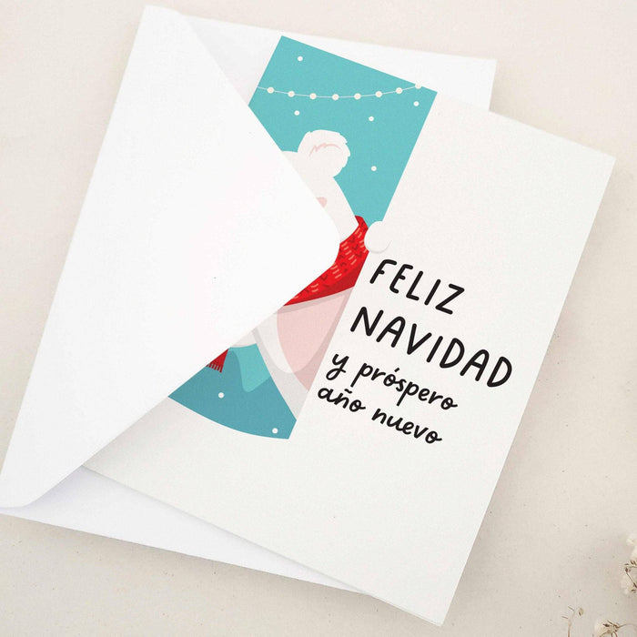 Folded holiday card featuring polar bear illustration with red scarf, falling snow, and Spanish holiday greeting, displayed with envelope — XOXOKristen.