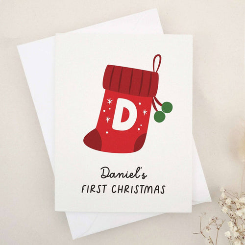Personalized First Christmas card with red stocking design and holly leaves, paired with white envelope – XOXOKristen