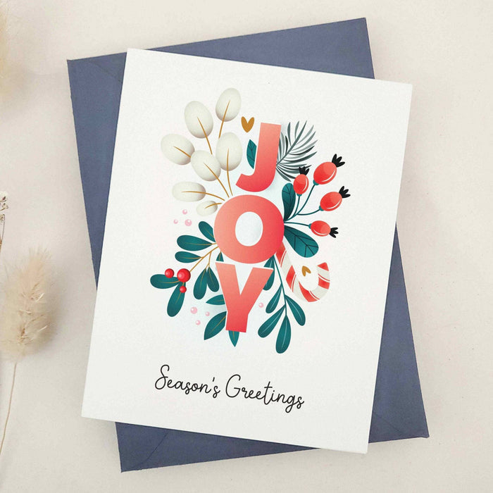 Standing card with “JOY” floral design and “Season’s Greetings” text, displayed with a coordinating envelope — XOXOKristen.