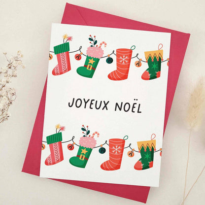 Standing card with stocking garland design, vibrant red and green tones, and “Joyeux Noël” message, styled with red envelope — XOXOKristen.