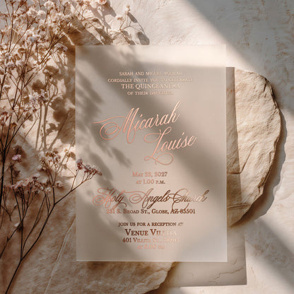 XOXOKristen translucent acrylic Quinceañera invitation with shimmering rose gold foil lettering, placed on textured beige stone with dried florals and natural light shadows, perfect for a modern 15th birthday – XOXOKristen.
