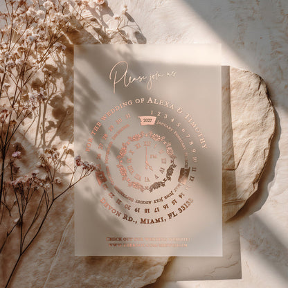 Romantic vellum wedding invitation with rose-gold foil details and round clock motif, styled with dried florals and warm sunlight – XOXOKristen