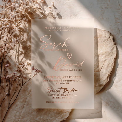 A personalized vellum wedding invitation featuring shimmering rose-gold foil text, blending modern elegance with romantic warmth. The design highlights the couple’s names in graceful script, complemented by clean serif fonts for the event details. The rose-gold tone adds a soft metallic glow against the translucent vellum base, perfect for chic and romantic weddings. – XOXOKristen