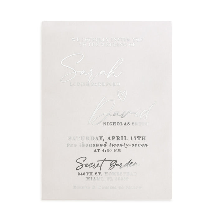 A translucent vellum wedding invitation with metallic silver foil lettering displayed on a natural stone surface beside delicate white blossoming branches. The light and shadows play beautifully across the frosted vellum texture, enhancing the reflective shimmer of the silver foil. The modern fonts and romantic layout create an elegant atmosphere, ideal for spring or garden weddings. – XOXOKristen